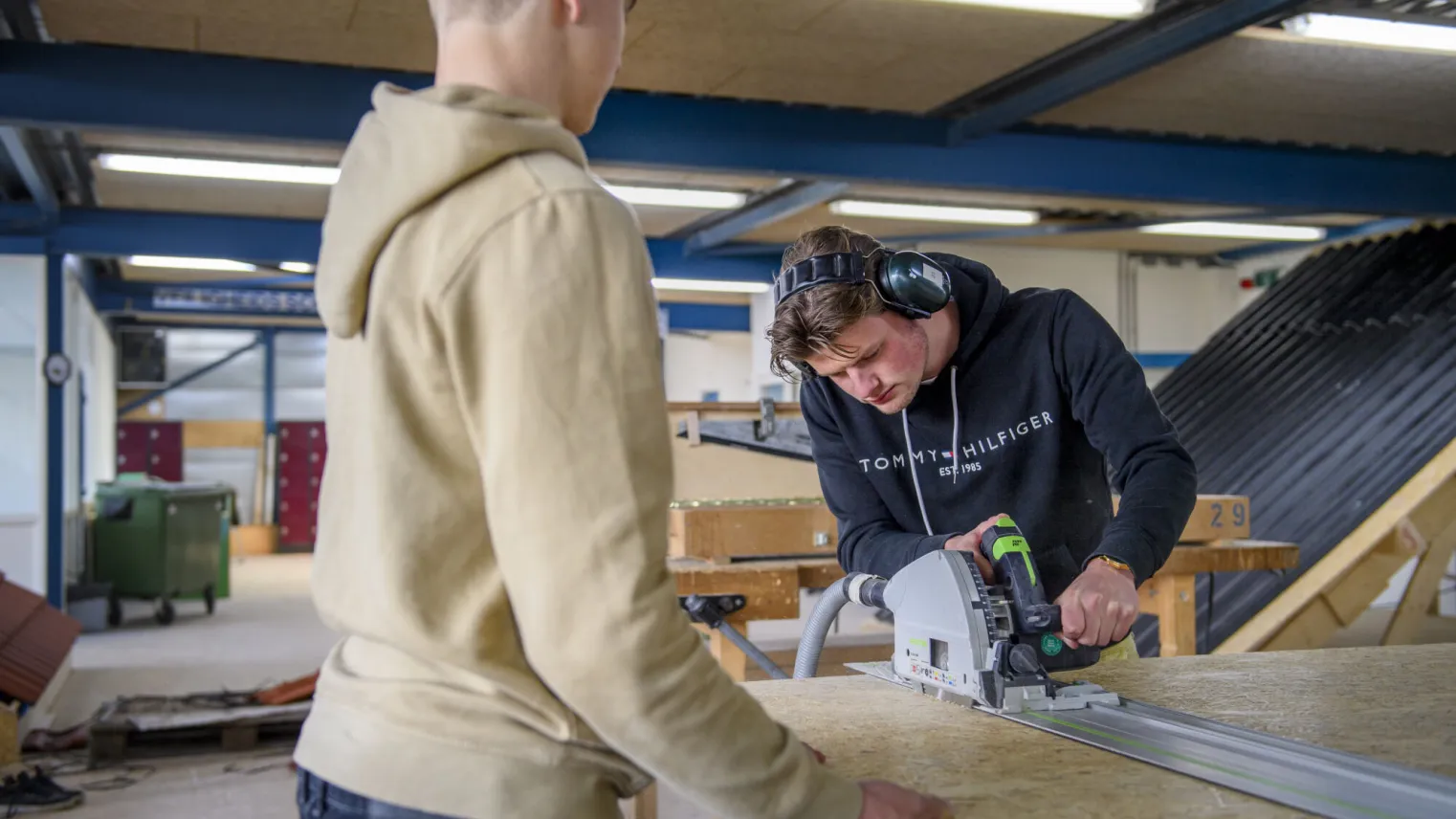 Studenten werken samen met een machine aan een object van hout