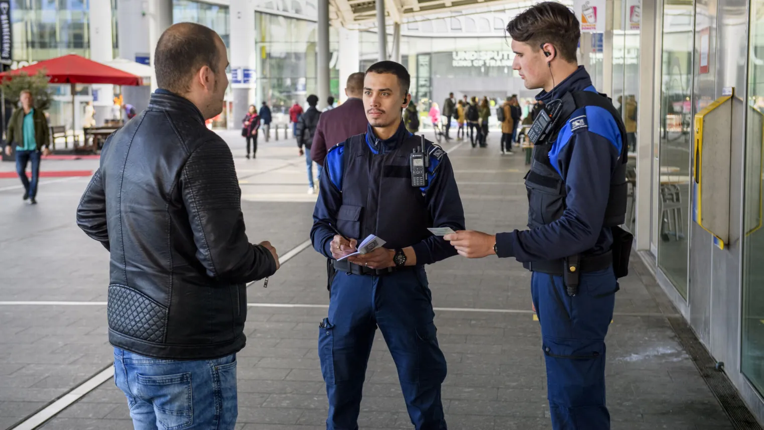 Twee handhavers in gesprek met man op straat.