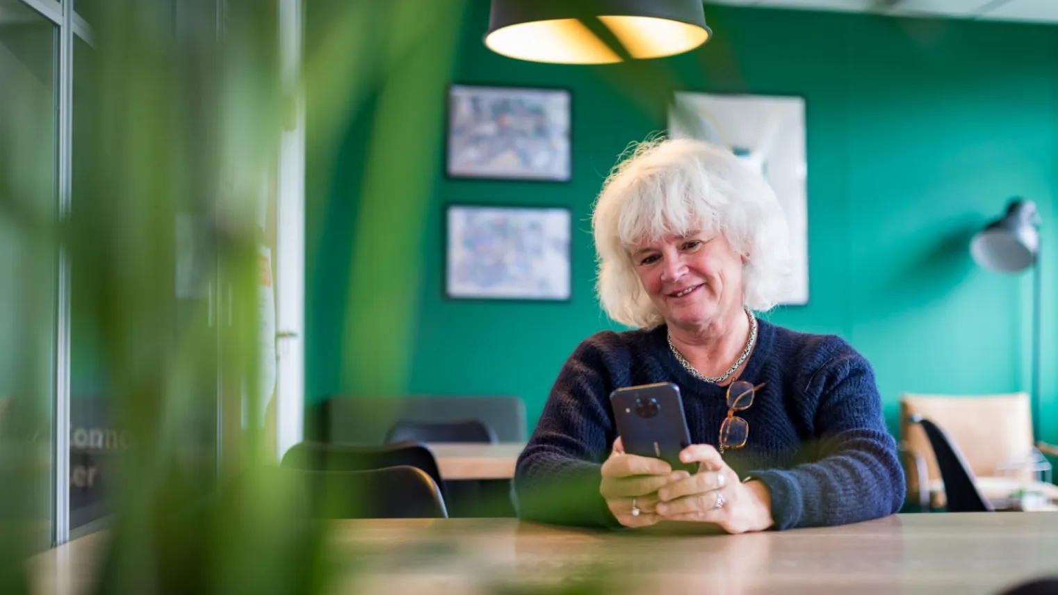 Vrouw zit in woonkamer en stuurt via mobiele telefoon gegevens door voor thuismonitoring.