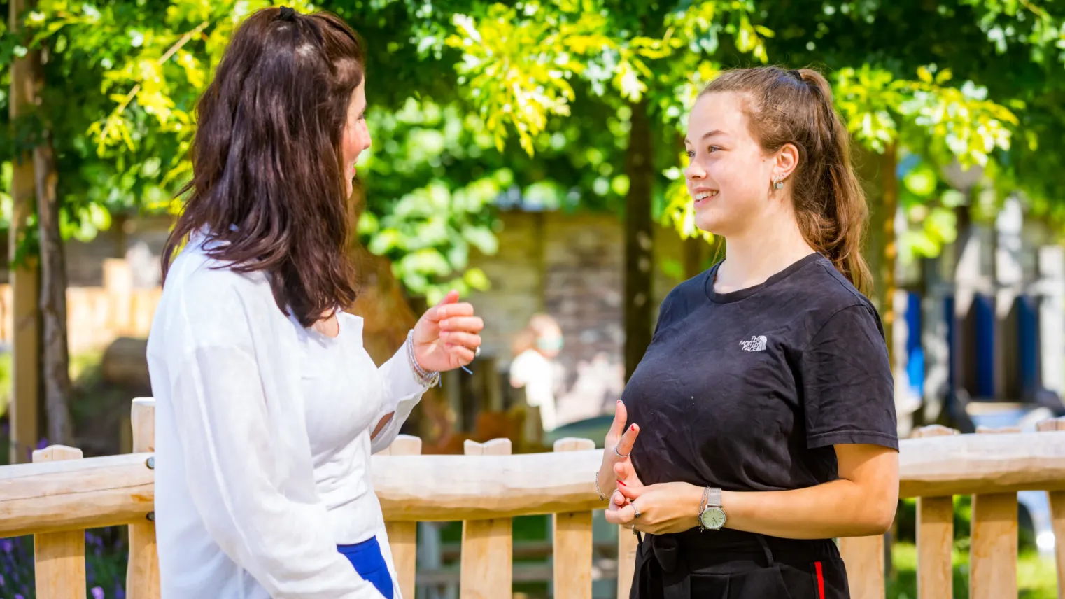 Twee vrouwen praten met elkaar naast een houten hek.