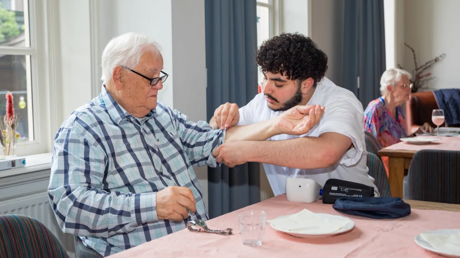 Student opleiding Verzorgende-IG controleert bloeddruk van oudere man. 