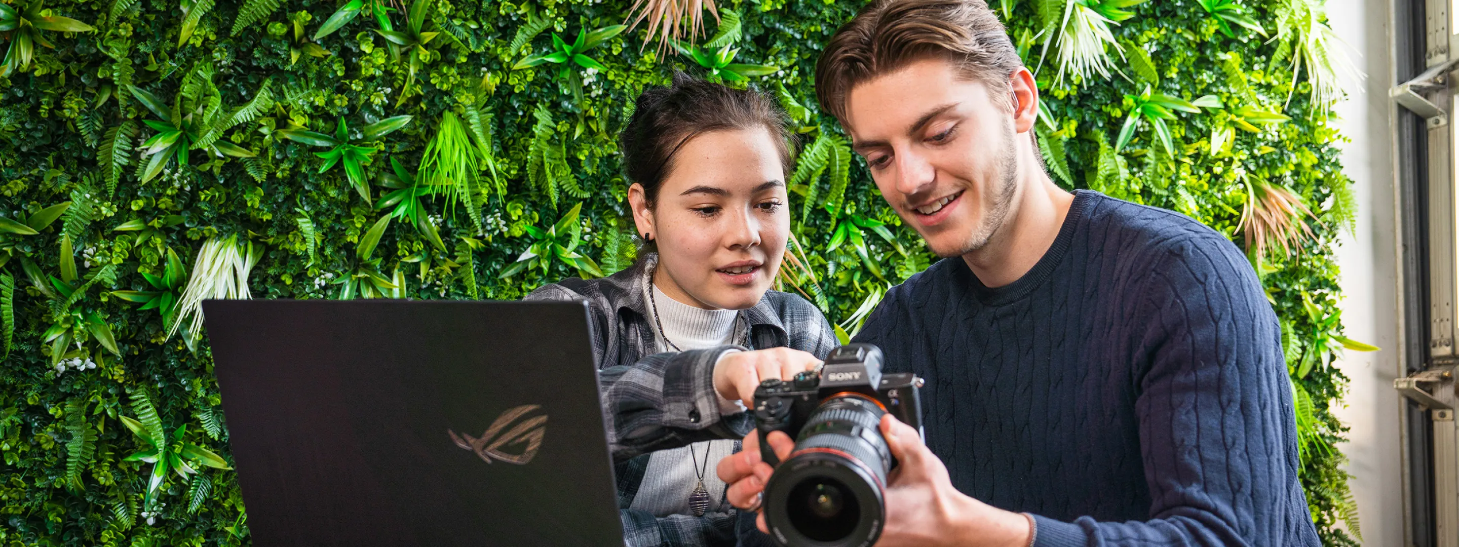 Twee studenten bekijken foto's op een camera met laptop erbij