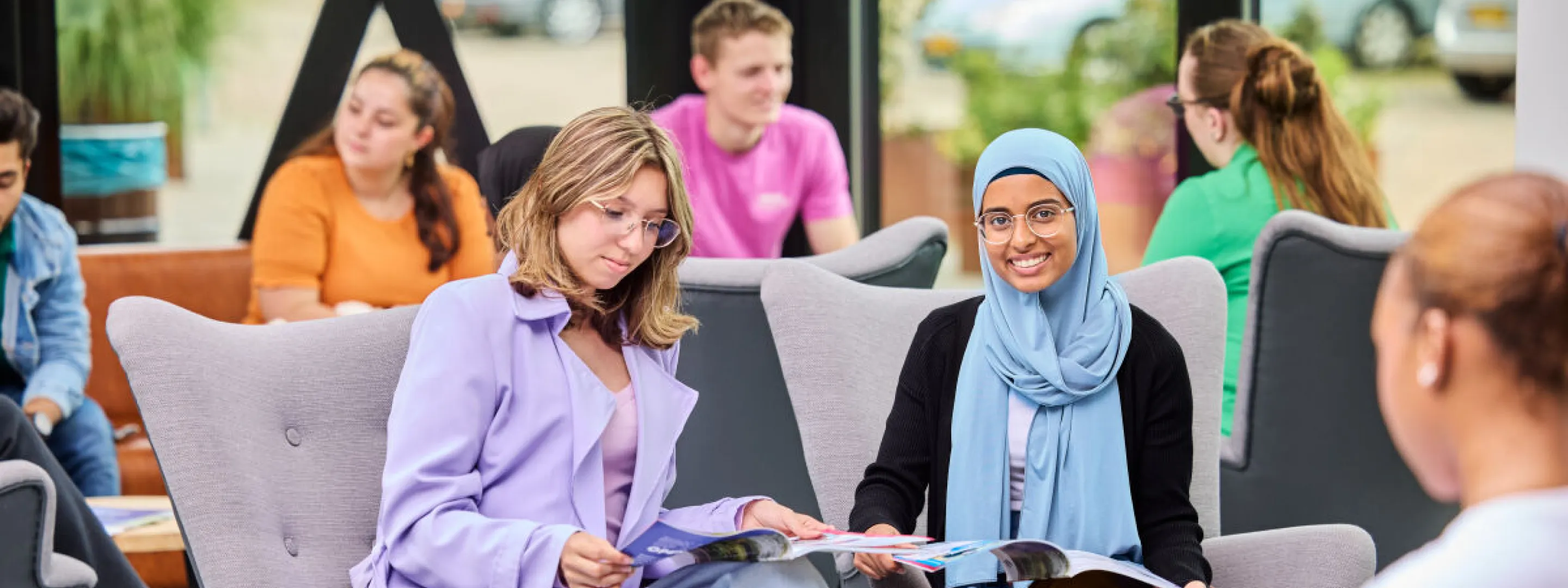 Twee studenten op grijze stoelen lezen een studiekeuzegids