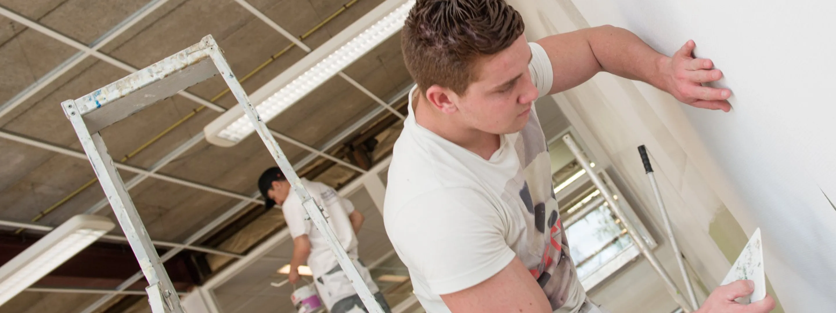 Een man schildert een muur met witte verf.