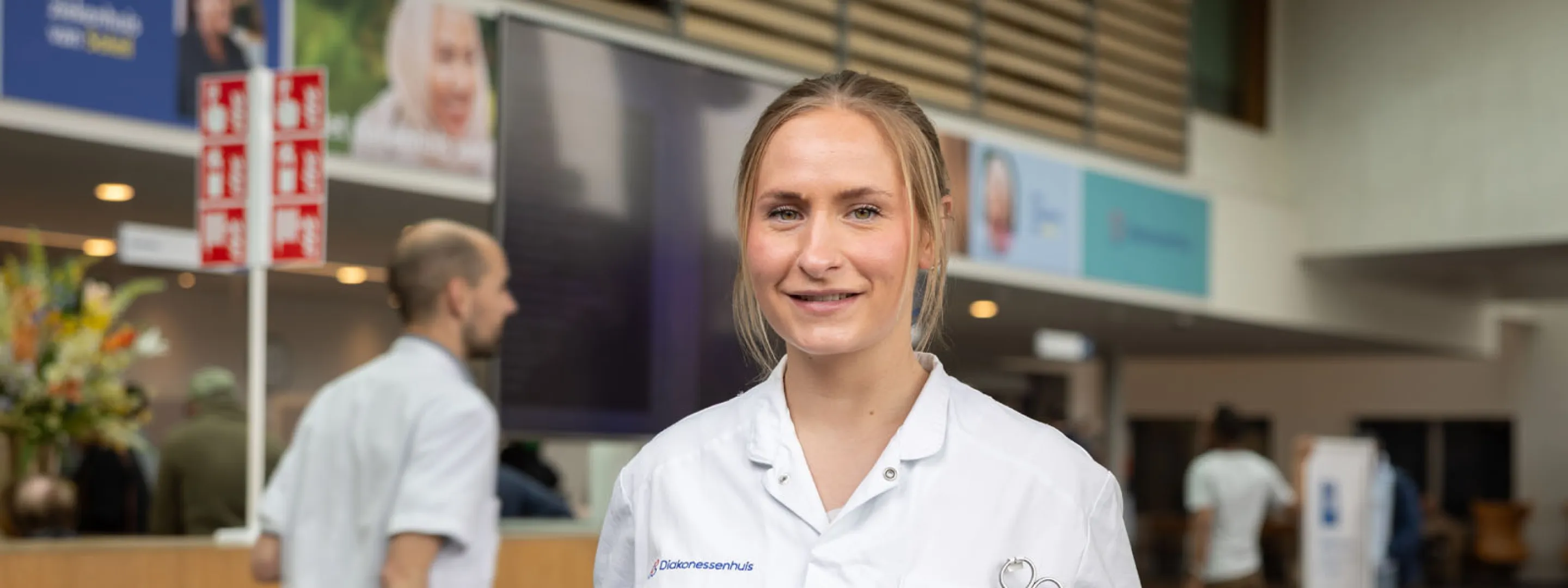 Naomi van Toor, oud-student opleiding Doktersassistent, staat voor balie in ziekenhuis.