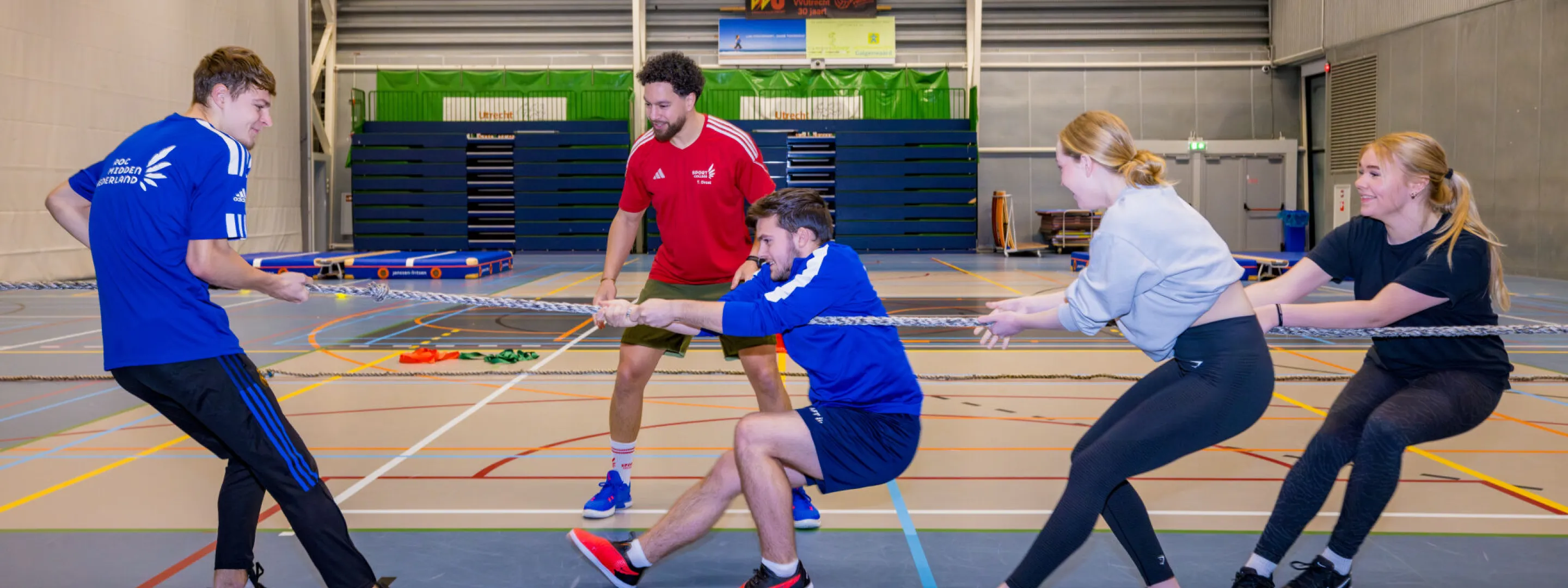 Een groep mensen speelt touwtrekken in een overdekte gymzaal.