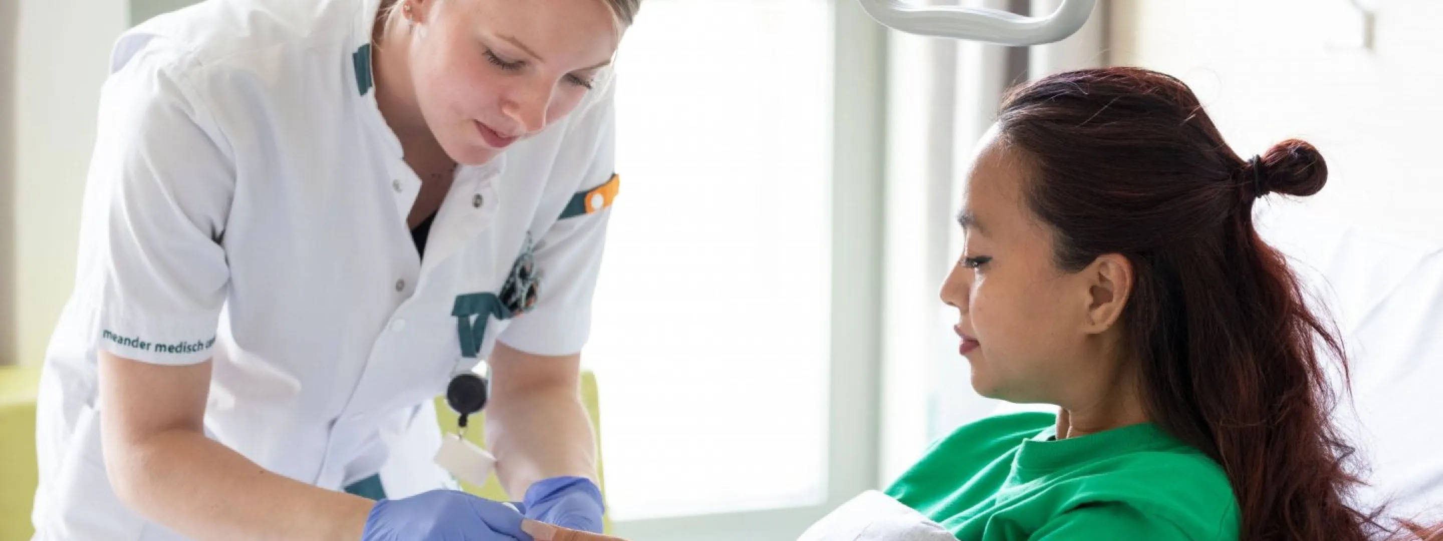 Een student Verpleegkunde prikt bloed bij een patiënt die in ziekenhuisbed ligt. 