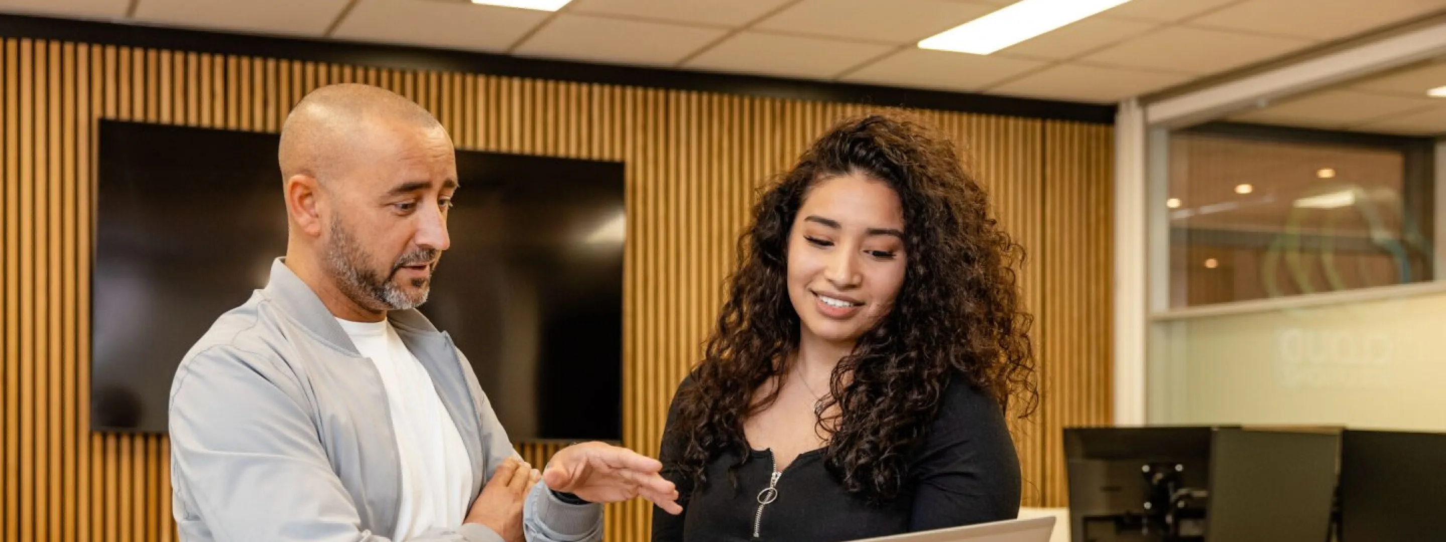 Student met laptop in haar hand aan het overleggen met docent.