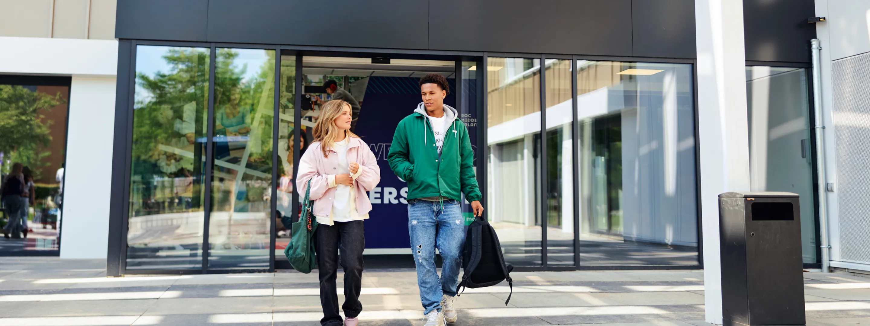 Twee studenten lopen bij de ingang van een schoolgebouw