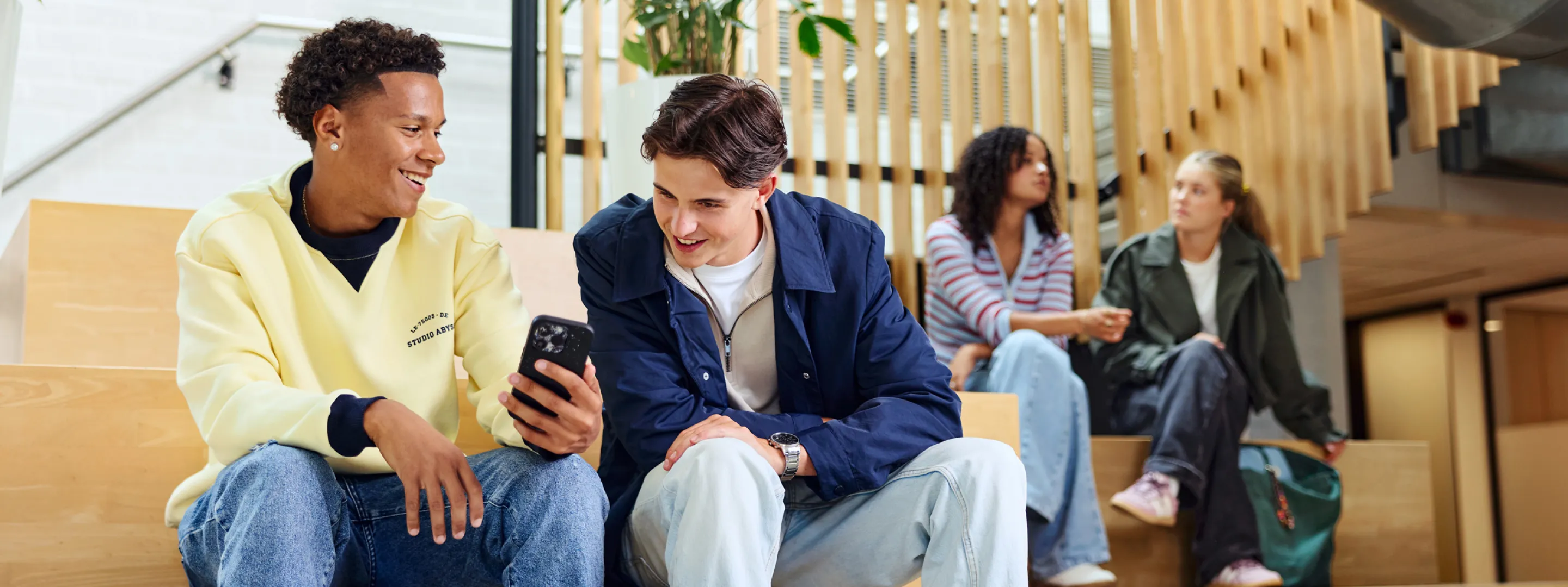 Twee studenten zitten samen op een bank en kijken naar een telefoon