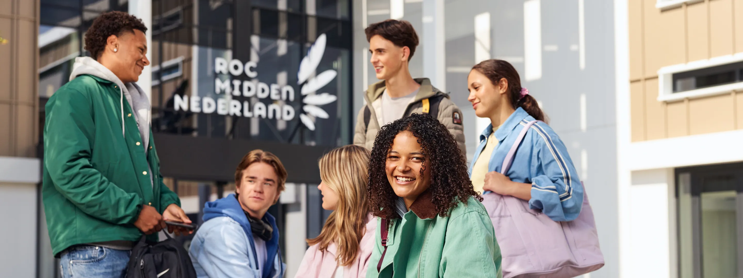 Groep studenten zit en staat buiten voor een schoolgebouw
